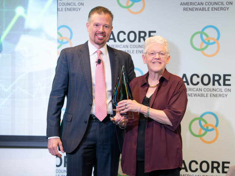 ACORE CEO and Gina McCarthy smile for a photo on stage. Gina holds an award.