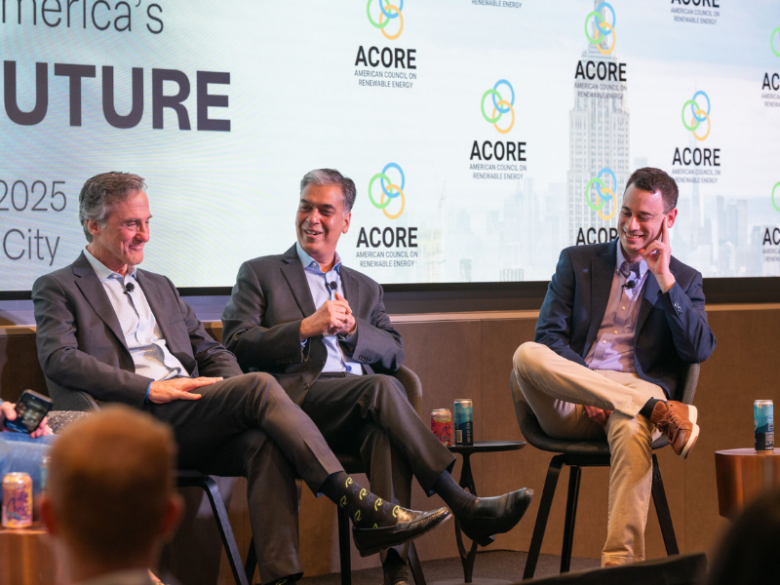 Three ACORE Finance Forum panelists smile on stage as they address attendees.