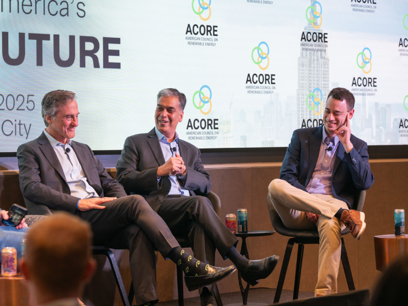Three ACORE Finance Forum panelists smile on stage as they address attendees.