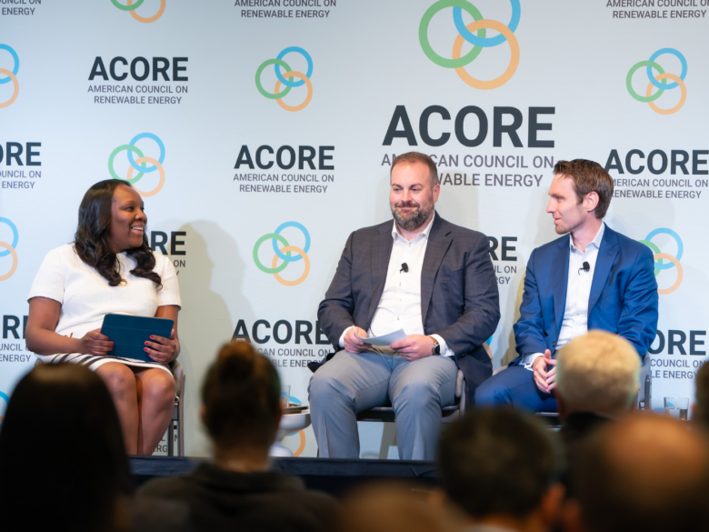 Three attendees sit on stage and address attendees at the ACORE Finance Forum
