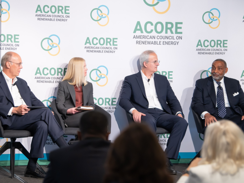 Four speakers sitting on a stage in front of an audience with the ACORE logo on a backdrop behind them.