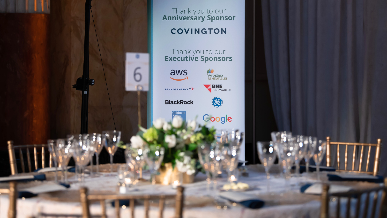 Gala sign displaying sponsors and table with flower centerpiece and cutlery.