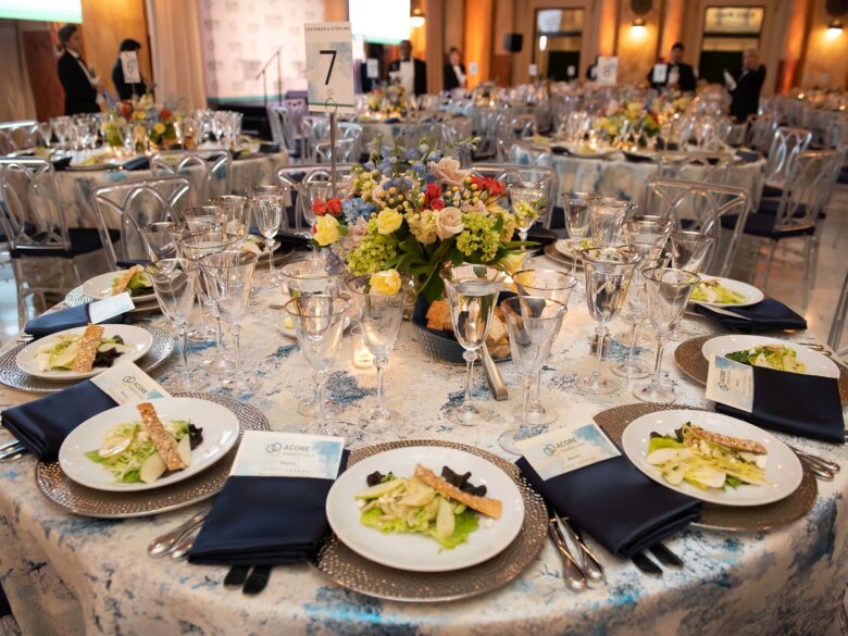 A round table with silver plates, yellow flowers, and silverware.