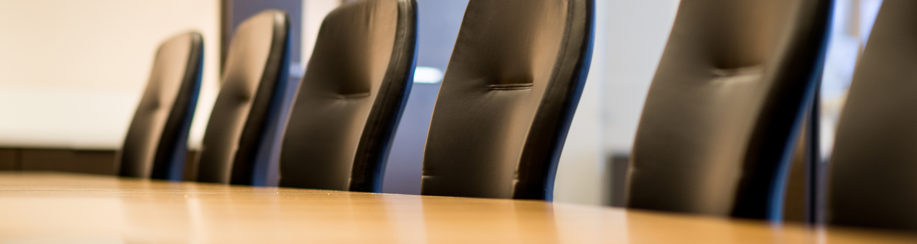 Several empty black leather office chairs around a board table.