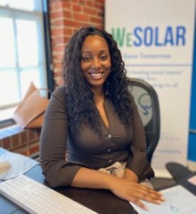 Kristal Hansley sitting at desk in front of sign that reads, "WeSolar"