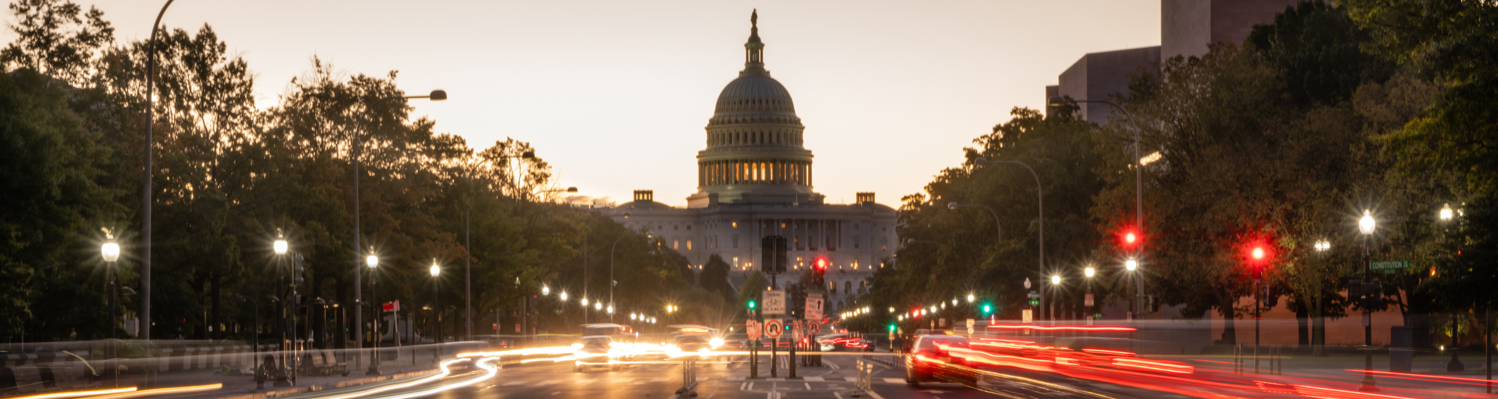 The US Capitol building at dusk at the end of a busy city street.