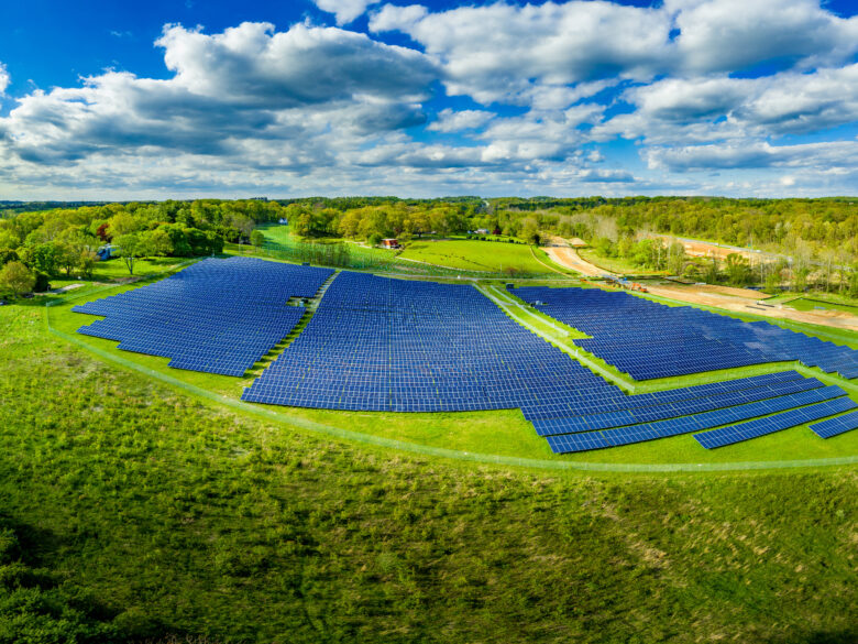 Aerial view of large solar farm with hundreds of blue solar panels as the sun reflects with cloudy blue sky in Maryland USA