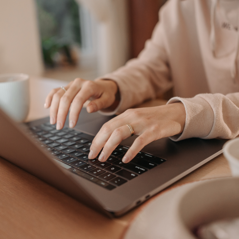 A woman typing on a laptop with a cup of coffee.