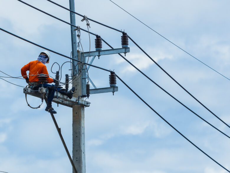 Electrician in bright orange shirt working atop a pole