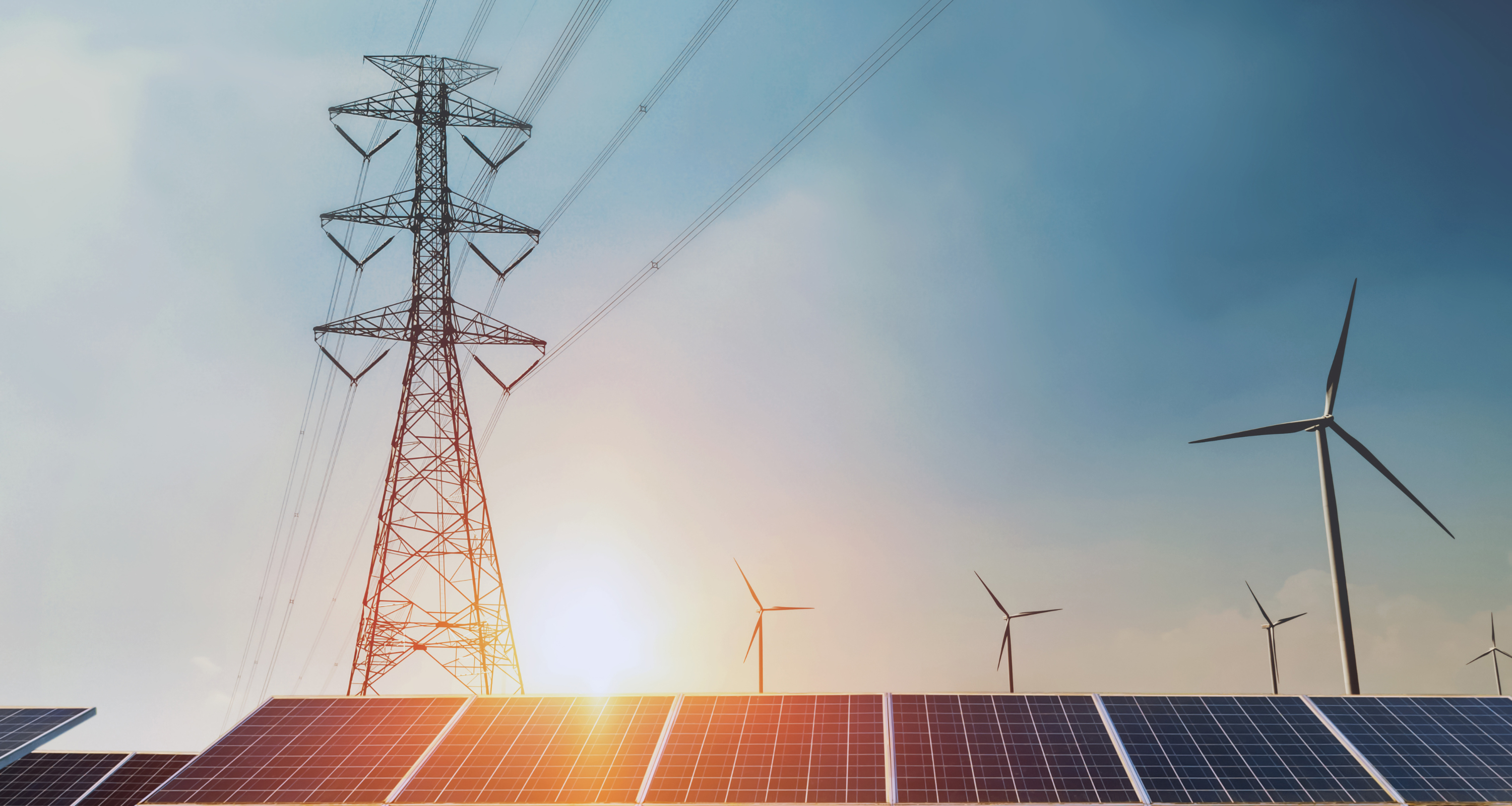 A transmission tower, wind turbines, and solar panels at sunrise