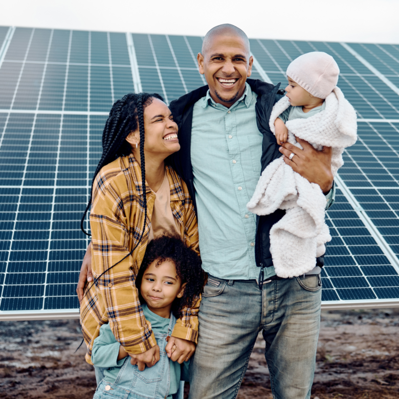 A family of four, with two young children, smiling and standing in front of solar panels.