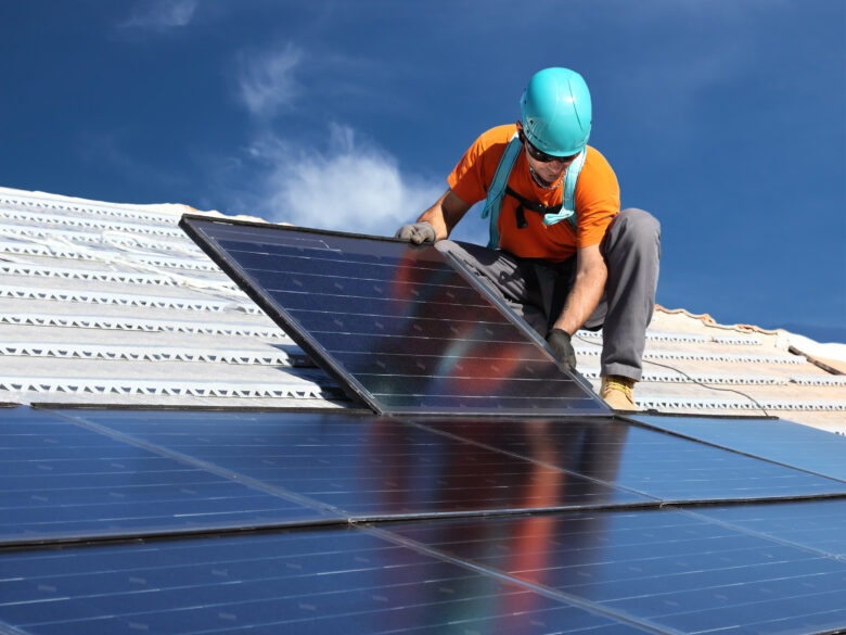 Worker in a hard hat installing a solar panel on a roof