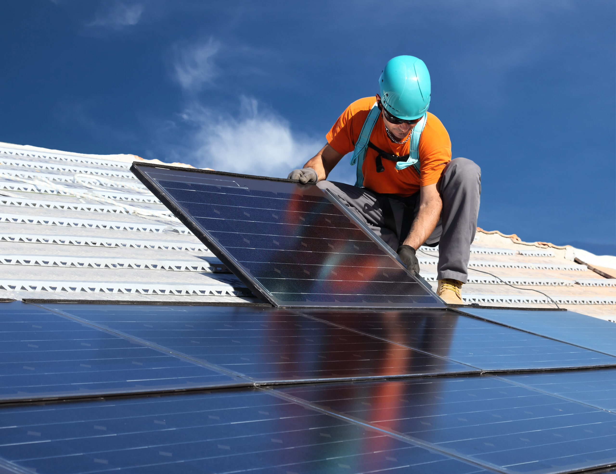 Worker in a hard hat installing a solar panel on a roof
