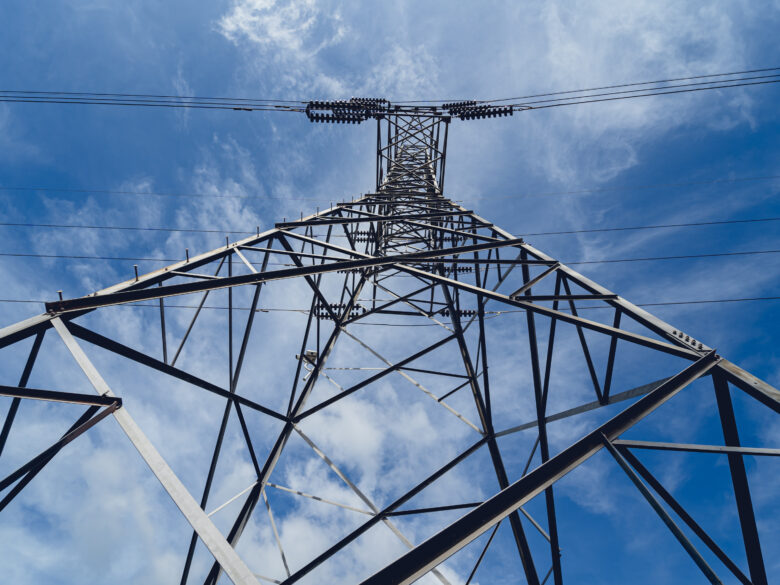 high voltage power transmission tower against a blue sky with white clouds