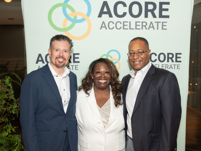 Three attendees pose in front of ACORE Accelerate photo backdrop.