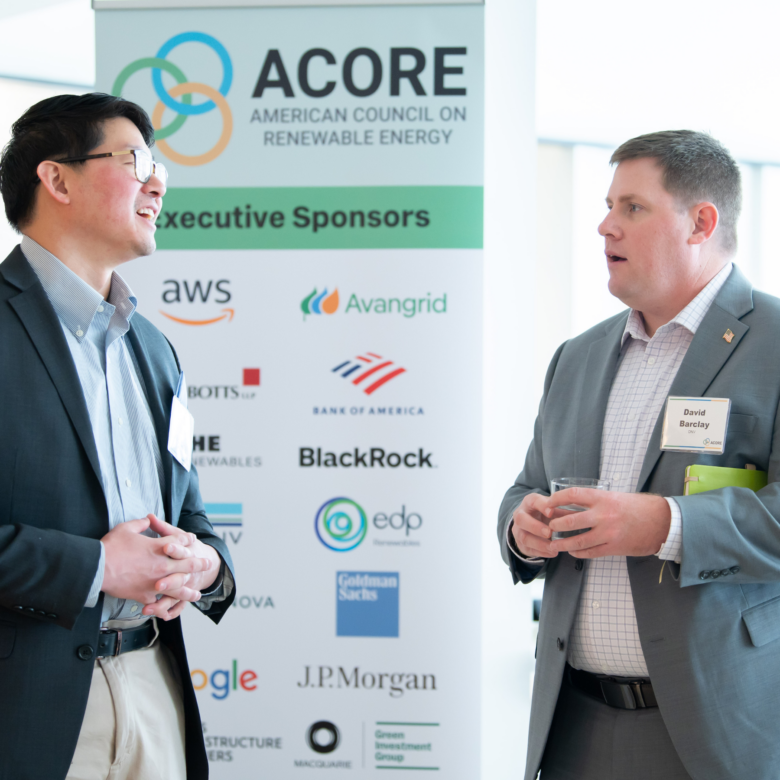 Two event attendees networking with a sponsor banner in the background.