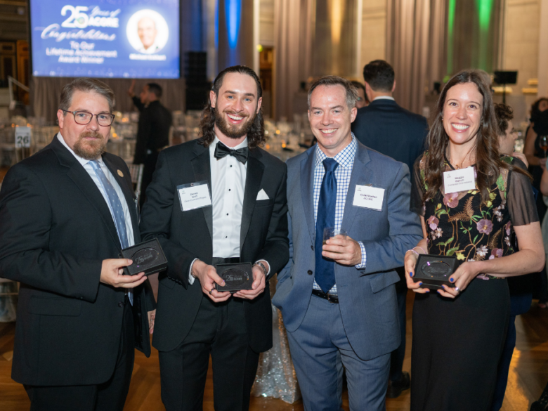 Four attendees pose for a photo while holding paper weights at the 25th Anniversary Gala.