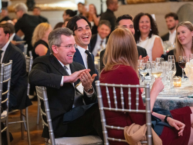 Attendees sit at their Gala table, smiling and laughing together.