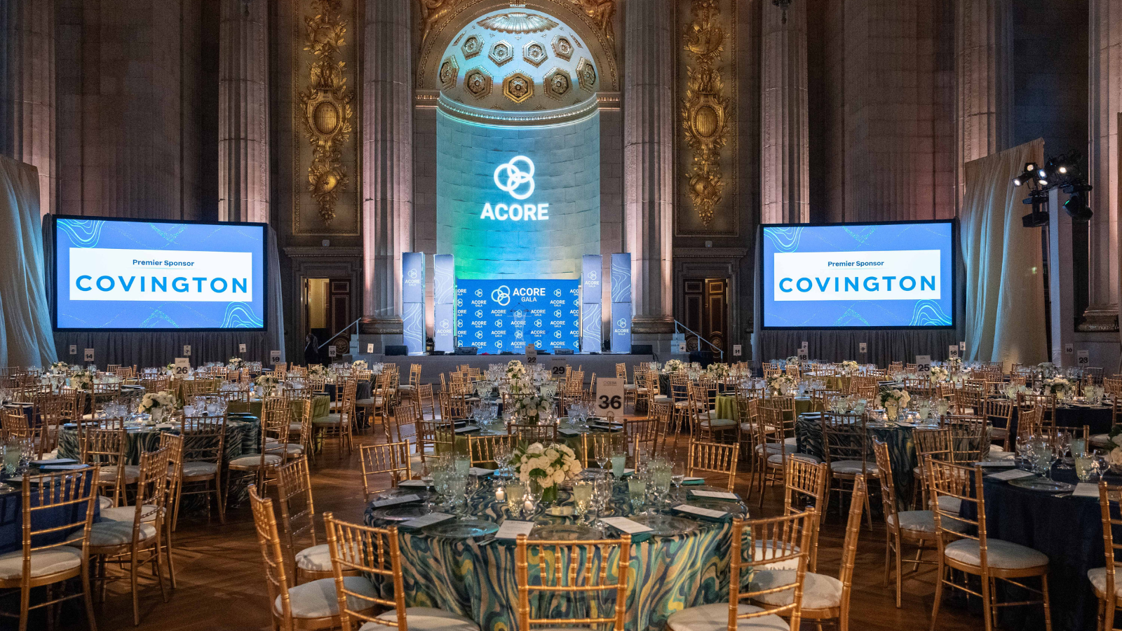 Room shot of the 2025 ACORE Gala at the Mellon Auditorium featuring set tables, screens, and the main stage.