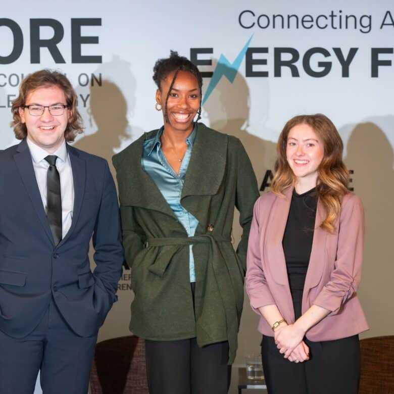 Three ACORE interns standing on stage at the ACORE Grid Forum smiling.