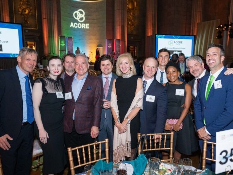 Group of 2025 ACORE Gala Attendees smiling for the camera at the Mellon Auditorium in front of the stage where the band is playing.