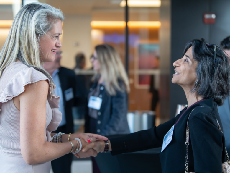 Two female attendees shaking hands at a networking event.