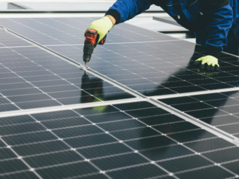 A close-up of a worker installing solar panels, using a power drill to secure the panels into place.