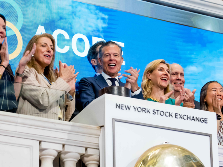A group of ACORE team and board members applaud behind the ceremonial bell podium at the New York Stock Exchange after ringing the Opening Bell.