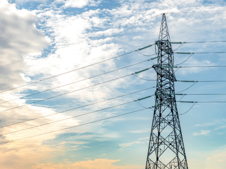 Transmission tower and power lines with sun and cloud background.