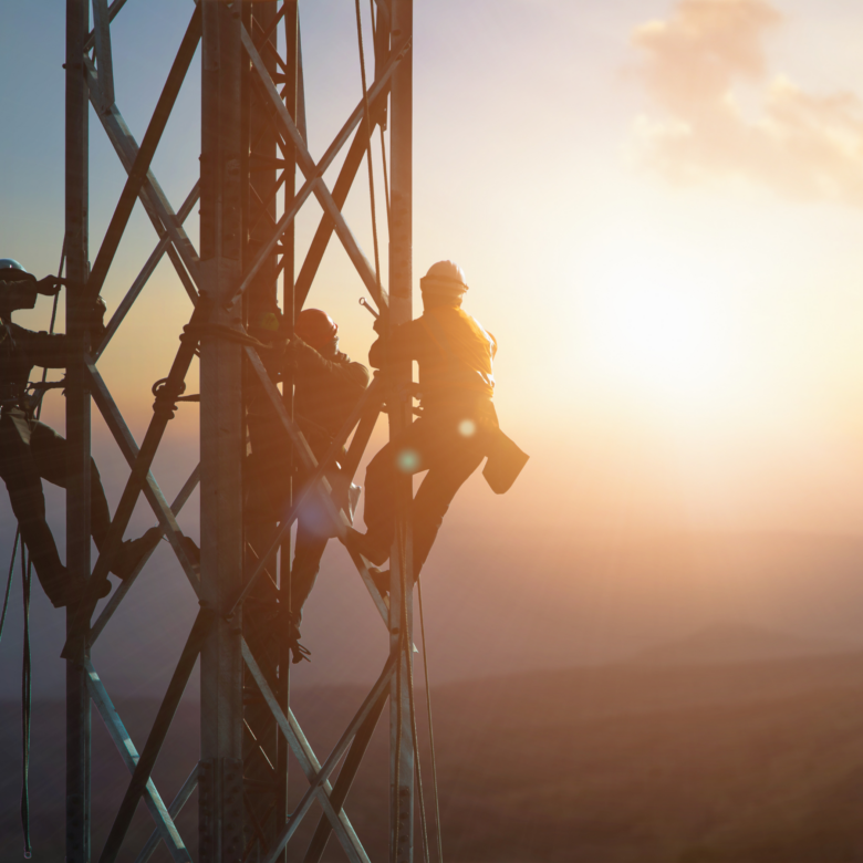 Three workers on a tower with a sunset background.