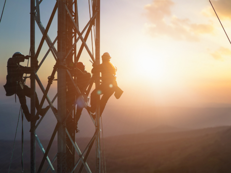 Three workers on a tower with a sunset background.