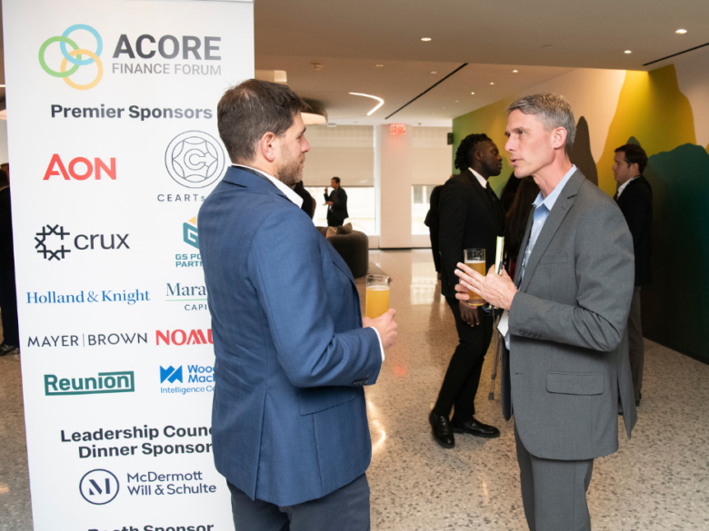 Two attendees networking beside a sponsor display at the ACORE Finance Forum.