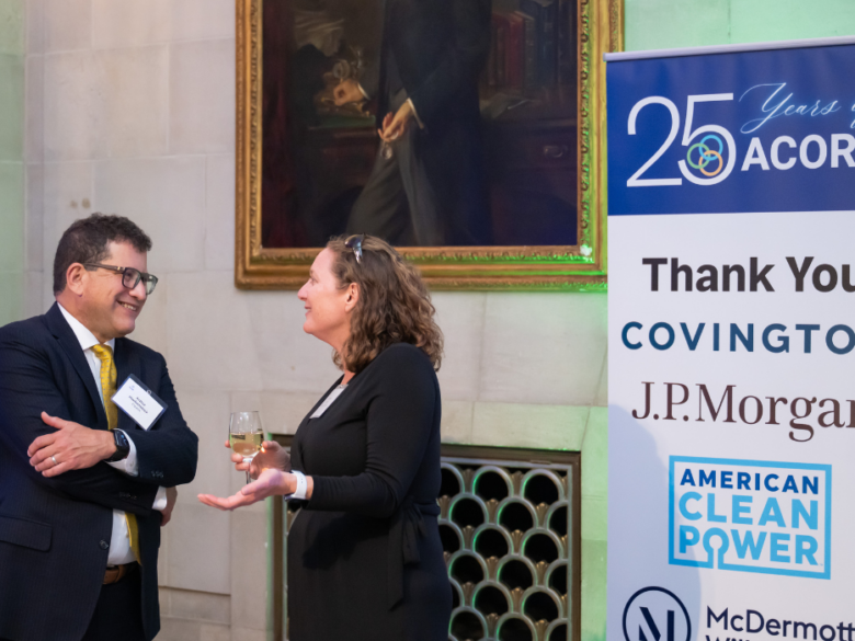 Two attendees talking beside a sponsor recognition banner during ACORE’s 25th Anniversary celebration.