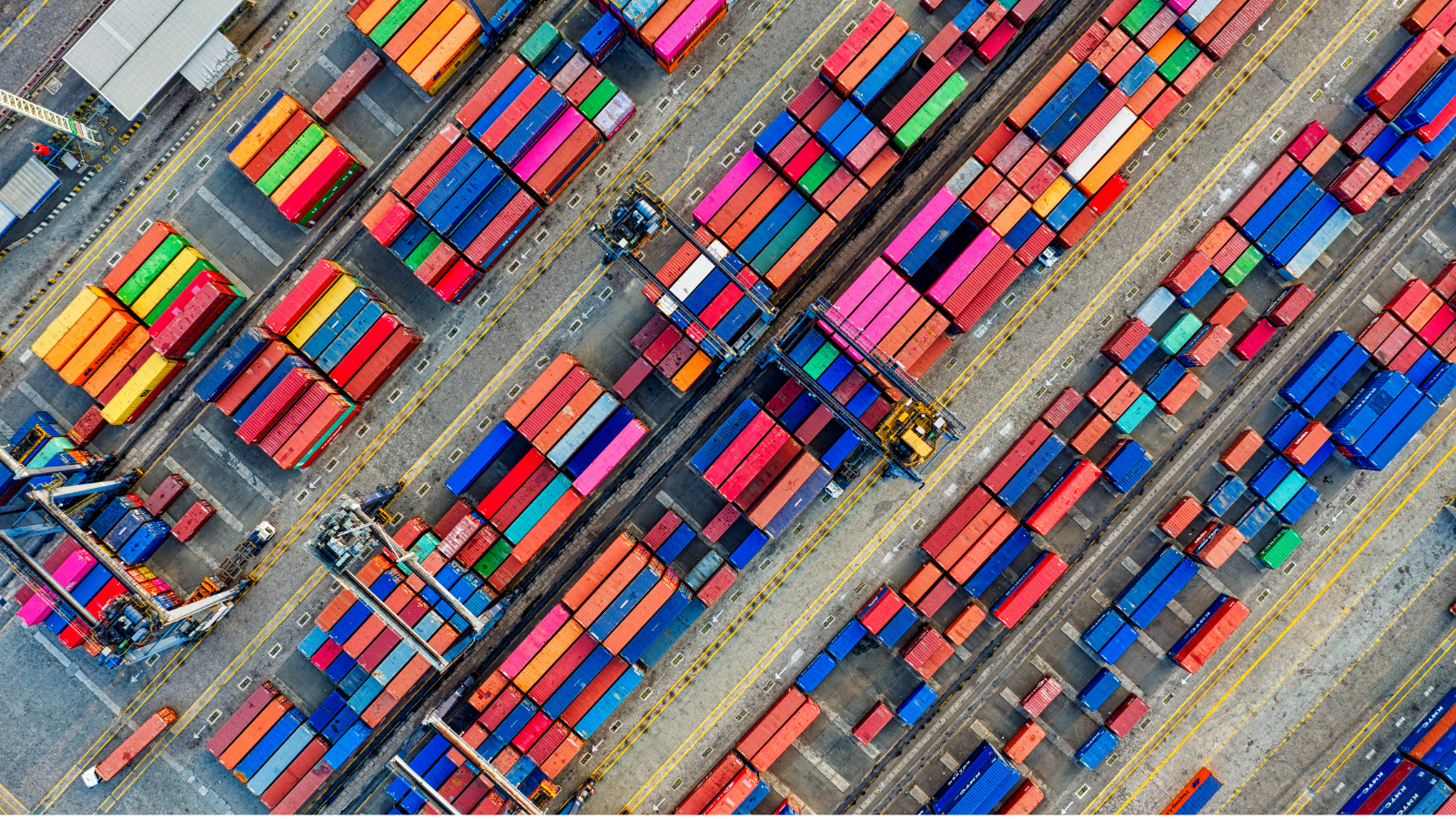 Aerial view of a shipping terminal with rows of colorful cargo containers, container-handling cranes, and marked transport lanes.