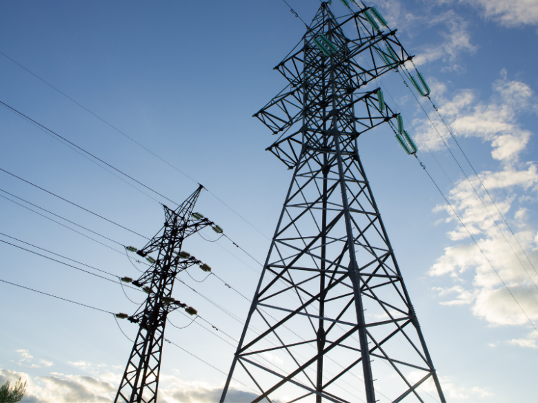 High-voltage transmission towers and power lines against a blue sky with scattered clouds.