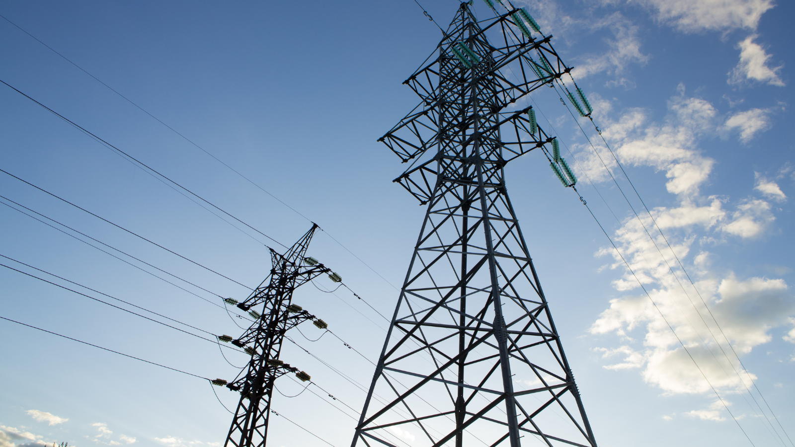 High-voltage transmission towers and power lines against a blue sky with scattered clouds.